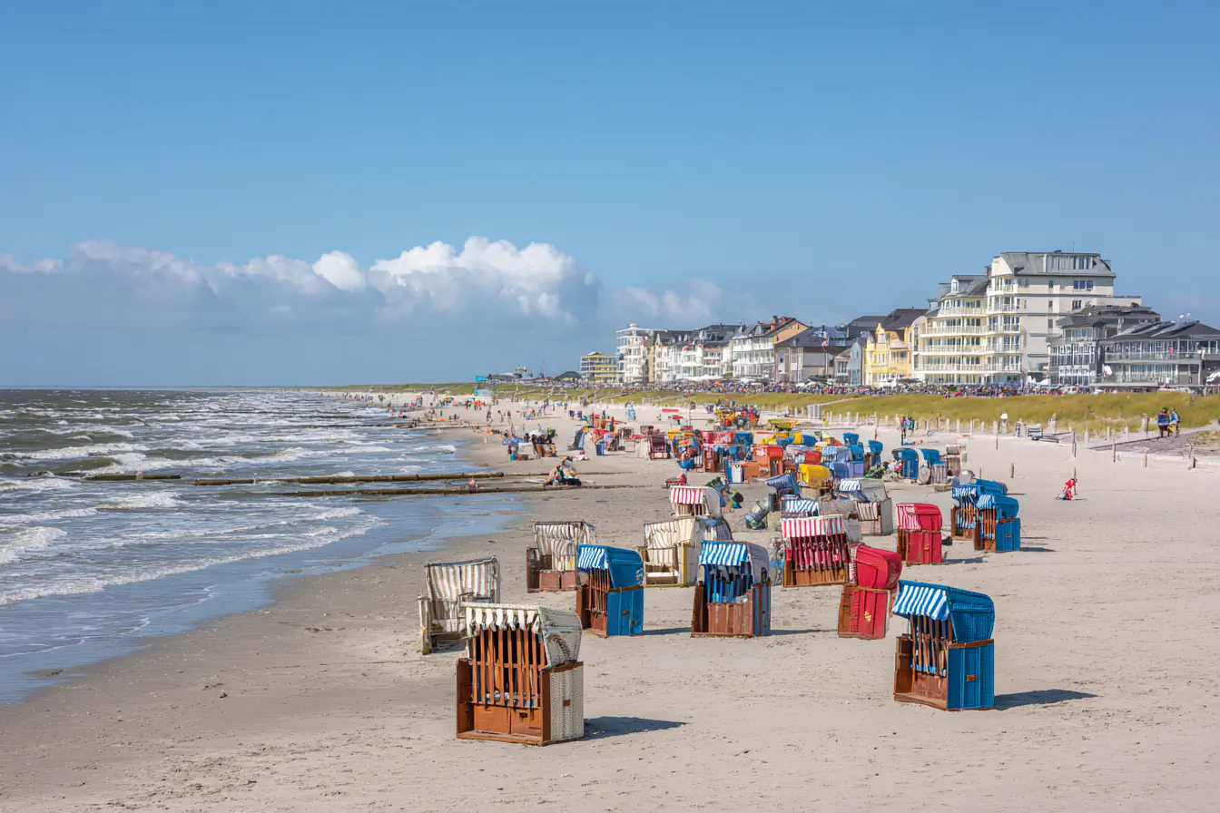 Strand von Norderney mit vielen bunten Strandkörben, Häusern und dem Meer.
